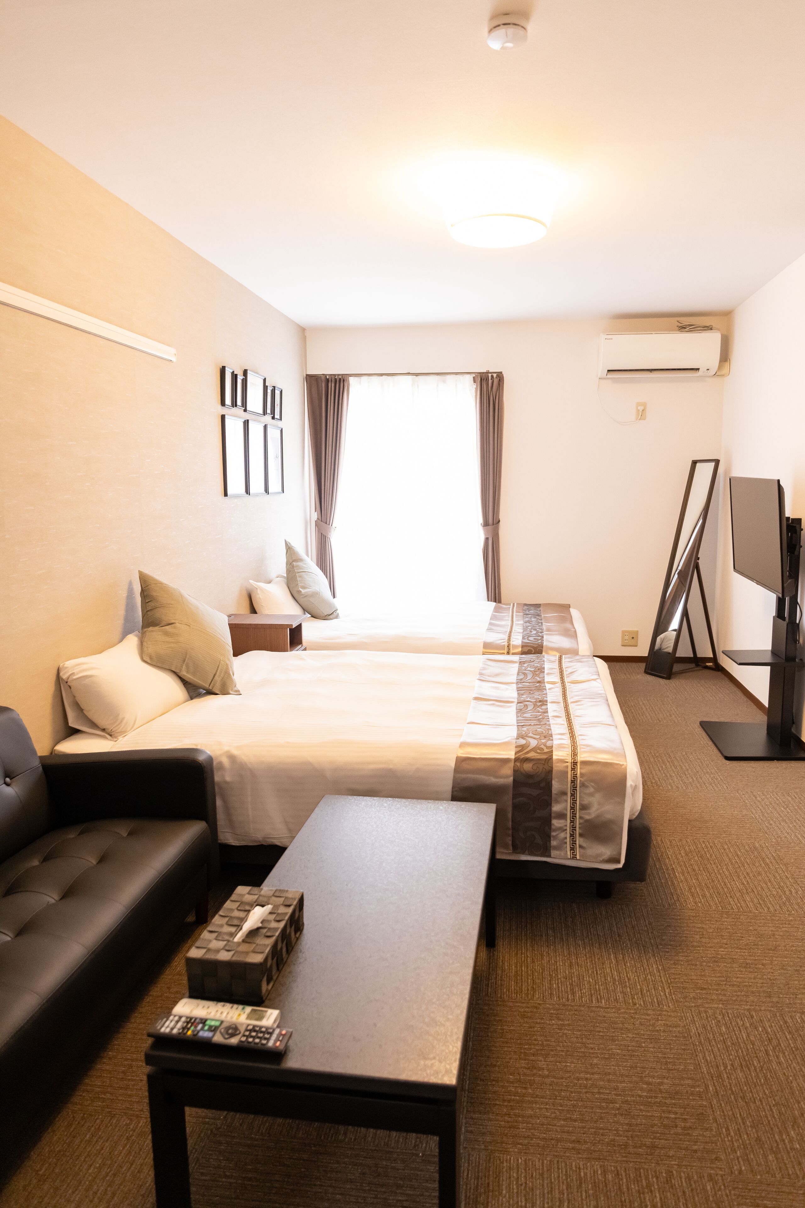 A hotel room with two beds, a sofa, a TV, and a flat-screen TV stand.