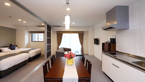 Een hotelkamer met een eettafel, twee bedden, een kitchenette en een groot raam.