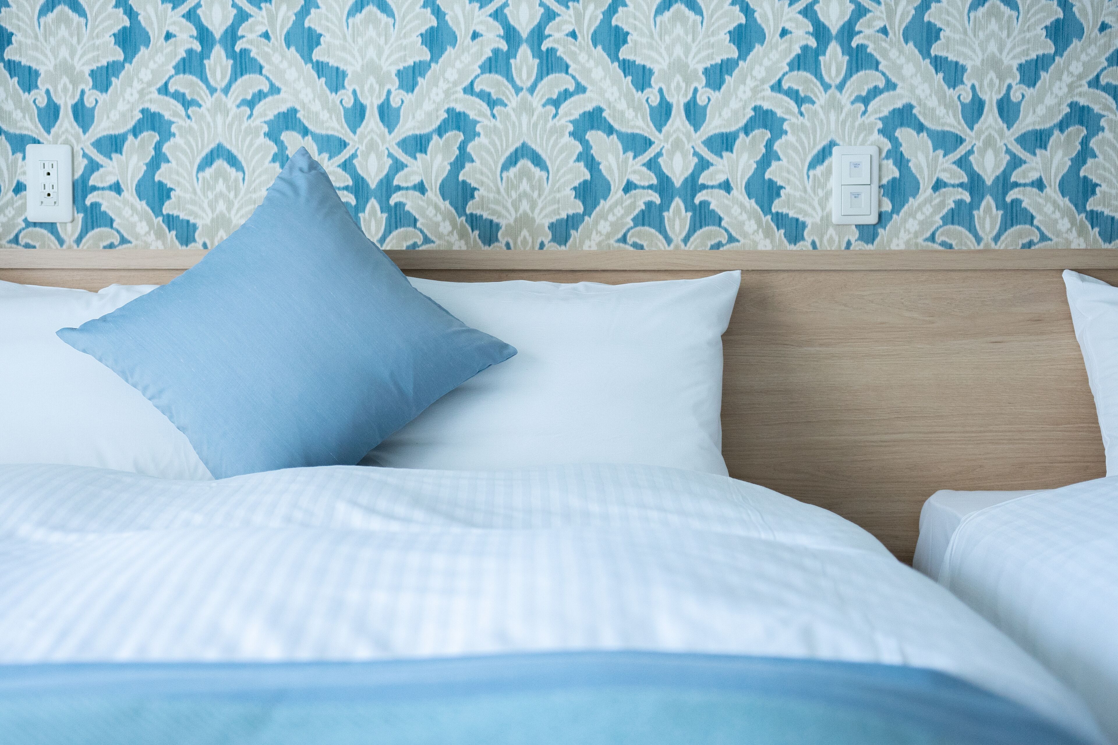 A neatly made bed with white and blue bedding, a wooden headboard, and a patterned wallpaper in blue and white.