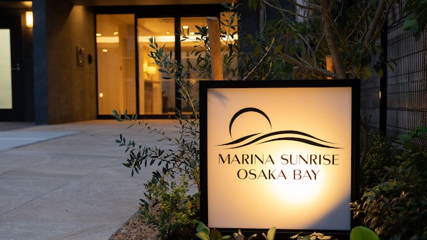 Een bord voor Marina Sunrise in de Baai van Osaka, met een modern gebouw op de achtergrond.