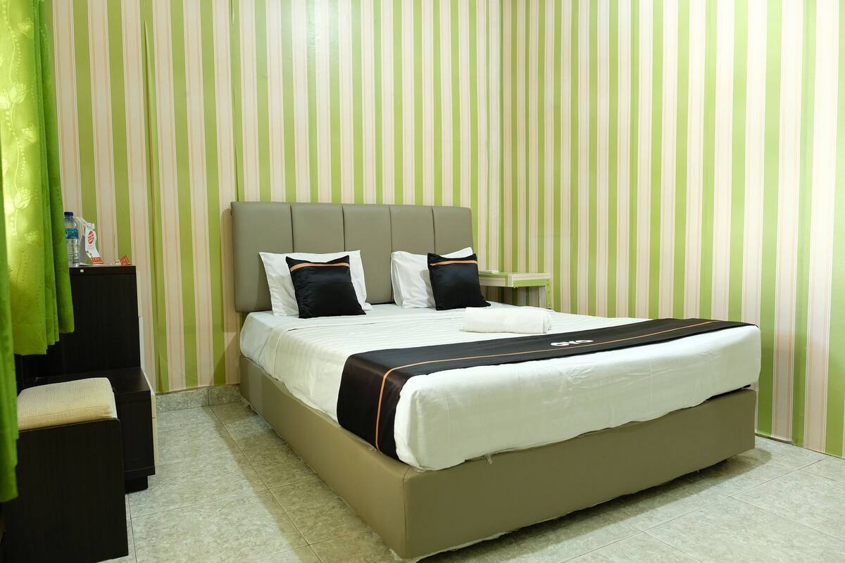 Een keurig opgeruimde hotelkamer met een groot bed, een nachtkastje en een groen gordijn.