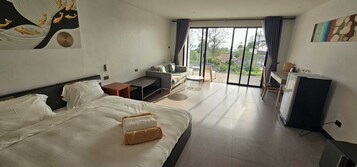 Habitación de hotel con una cama grande, un sofá, una mesita, un televisor y un balcón con vistas.