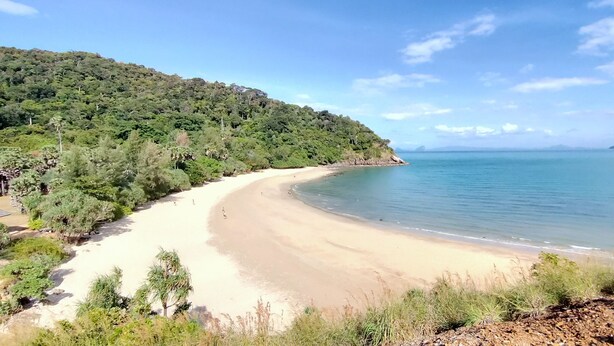 A beach with a curved shoreline, surrounded by dense green forest and a clear blue sky. - Aranya Resort Koh Lanta (Ko Lanta)