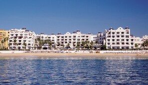 Ein Strandhotel mit mehreren weißen Gebäuden, Palmen und einem Sandstrand.