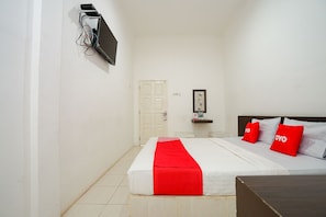A hotel room with a bed, a TV mounted on the wall, a door, and a small table with a picture frame. - Super OYO 1868 Penginapan Sekip (Palembang)