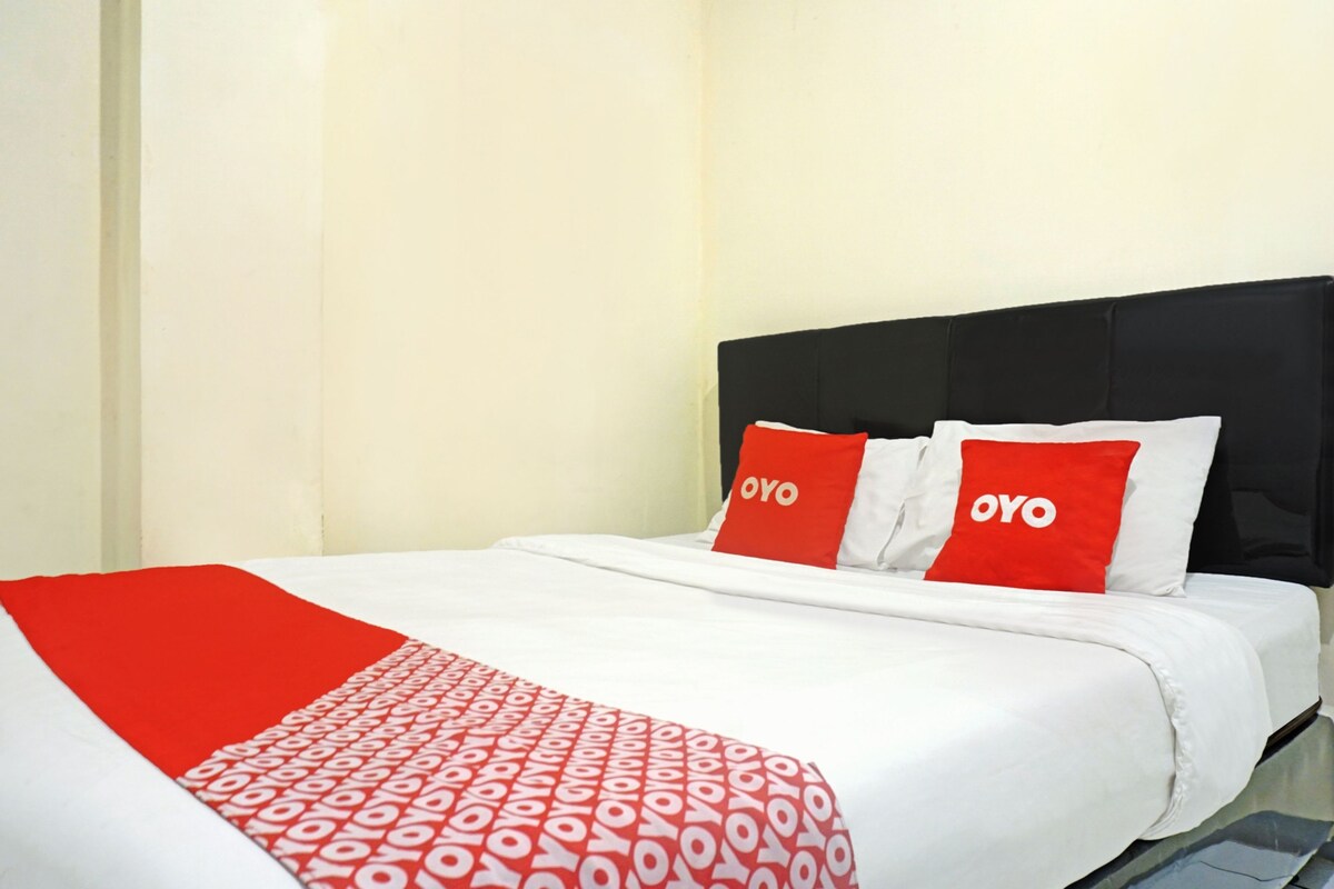 A hotel room with a bed, white bedding, and red and white pillows with the word "OYO" on them.
