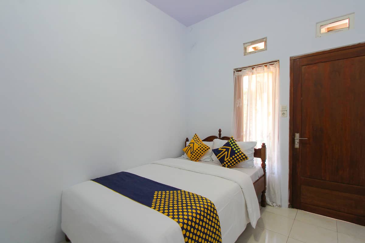 Un dormitorio pequeño y ordenado con una cama individual, una puerta de madera y una ventana con cortinas.