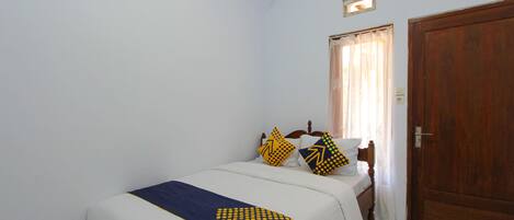 Un dormitorio pequeño y ordenado con una cama individual, una puerta de madera y una ventana con cortinas.