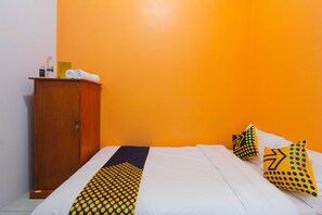 Une chambre d’hôtel avec une armoire en bois, un lit avec une literie blanche et des coussins à motifs jaunes, et un mur d’un orange vif.