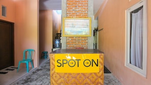 A hallway with a 'SPOT ON' sign, a blue chair, and a brick wall. - SPOT ON 2022 Darman Family Residence Syariah (Banyuwangi)