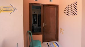 A hallway with a wooden door, a green chair, and directional signs. - SPOT ON 2022 Darman Family Residence Syariah (Banyuwangi)