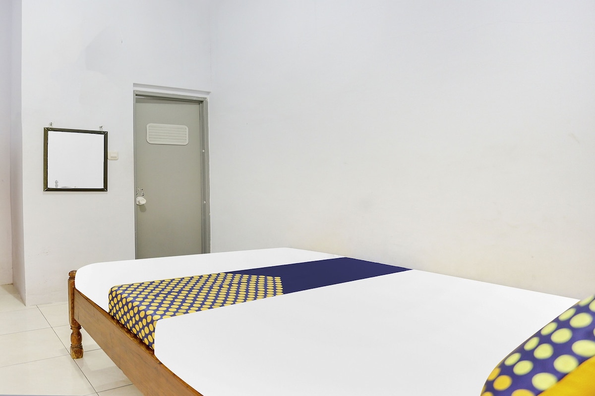 A single bed with a patterned bedspread, a door, and a wall-mounted light switch.