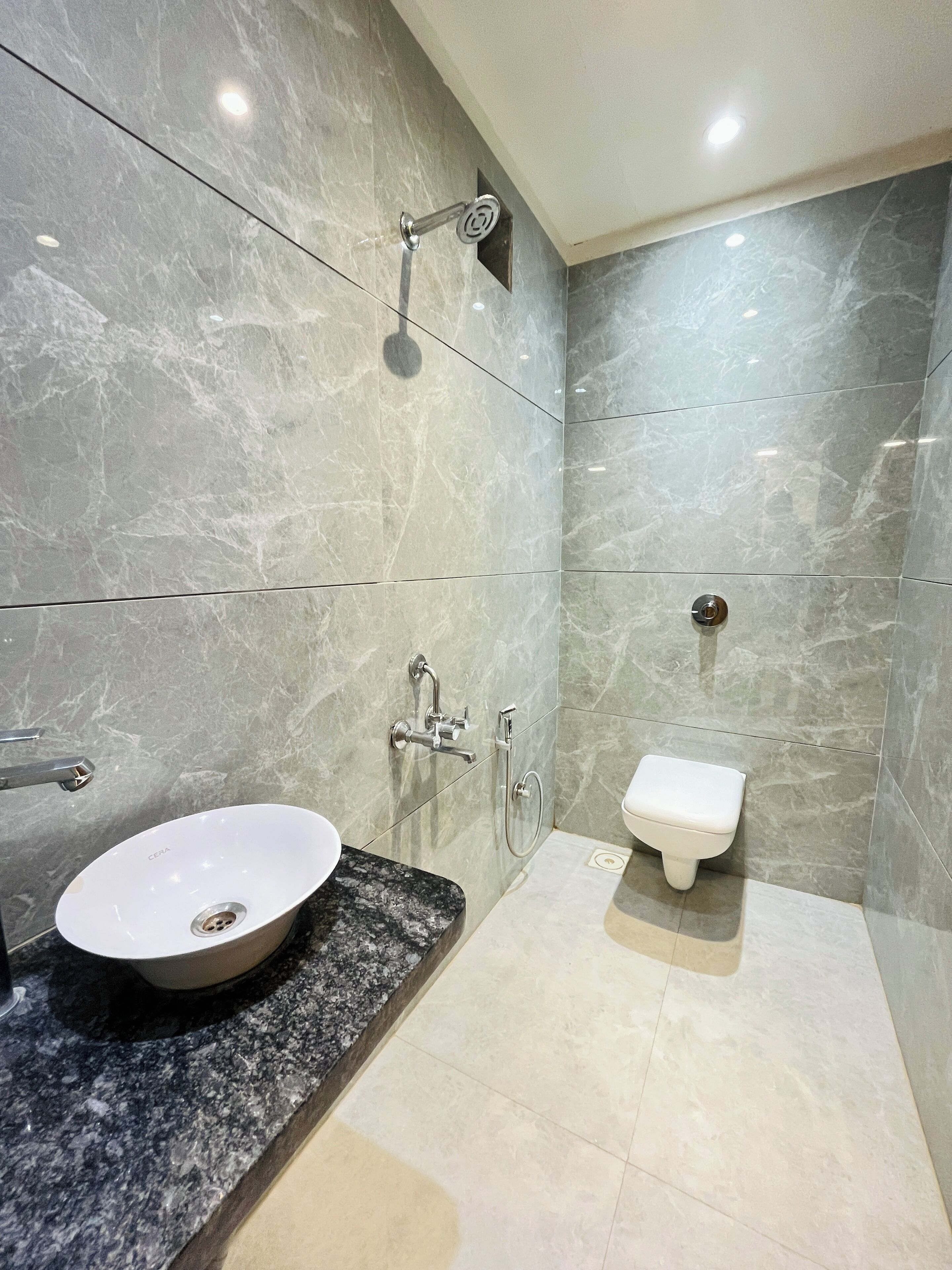 Une salle de bain moderne avec un lavabo en marbre, une douchette à main et des toilettes fixées au mur.