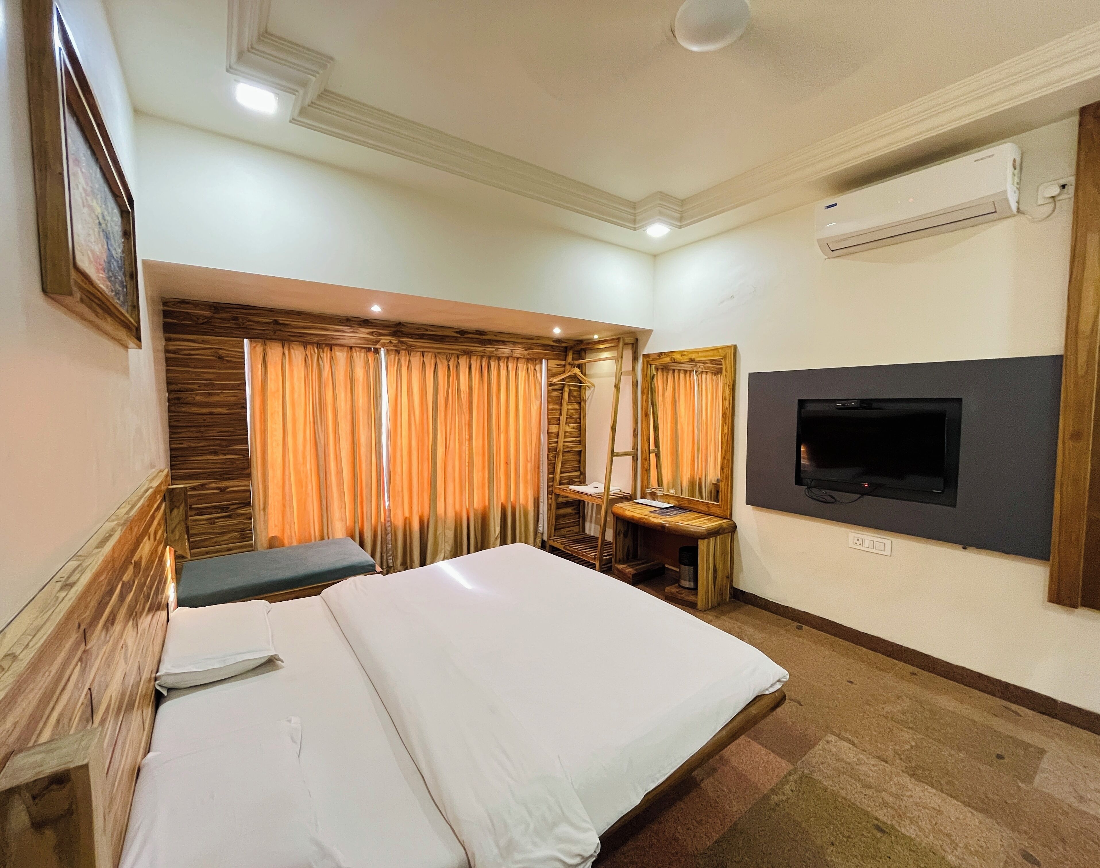 Une chambre d’hôtel avec un lit, une télévision, un bureau en bois et une grande fenêtre avec des rideaux.