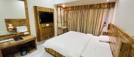 A hotel room with a wooden headboard, a large mirror, a flat-screen TV, a bedside table with a phone, and a window with curtains.