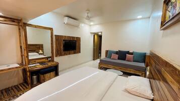 Habitación de hotel con cama de madera, sofá con cojines, televisor montado en la pared y ventilador de techo.