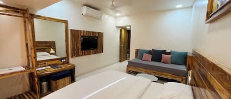 A hotel room with a wooden bed, a sofa with cushions, a TV mounted on the wall, and a ceiling fan.