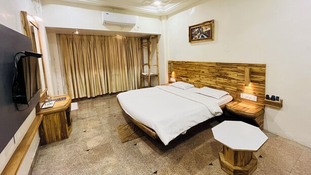 A hotel room with a large bed, wooden headboard, a small table, a TV, and an air conditioning unit. - Hotel Shripad Continental (Amravati)