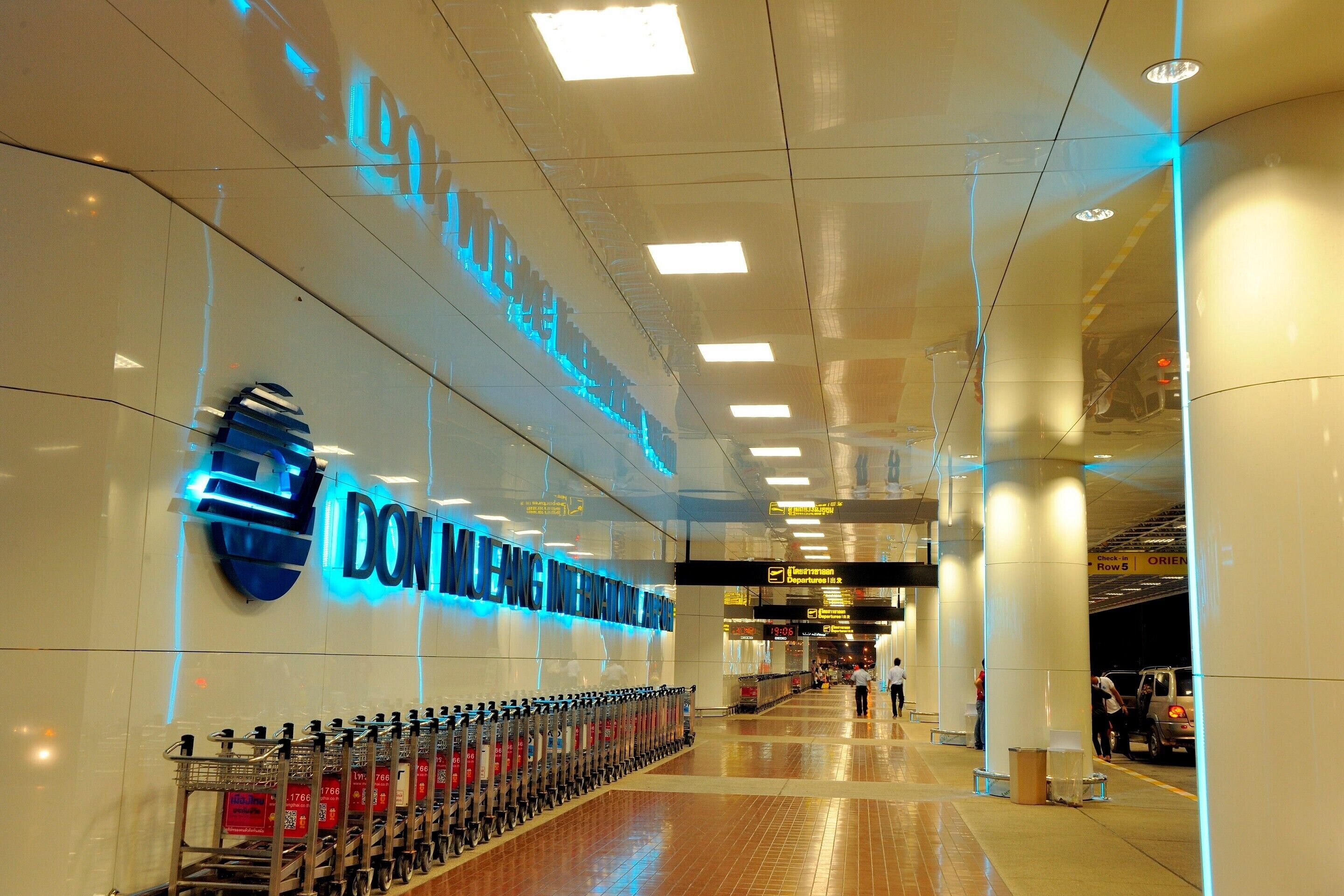 A spacious airport terminal with a clear walkway, a row of luggage carts, and a sign for Don Muang International Airport.