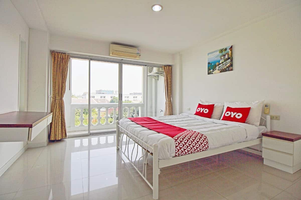 A hotel room with a bed, a desk, a balcony with curtains, and a painting on the wall.