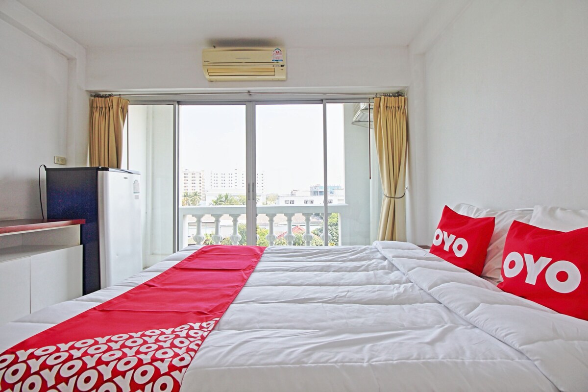 A hotel room with a bed, a TV, and a balcony with curtains.