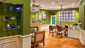 A dining area with a wooden table and chairs, a counter with a computer, and a green wall with framed pictures. - Club Mahindra Mount Serene Resort in Munnar (Devikolam)