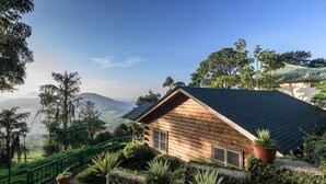 A wooden cabin with a sloped roof, surrounded by lush greenery and a scenic mountain view. - Club Mahindra Mount Serene Resort in Munnar (Devikolam)