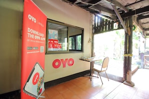 A hotel interior with a promotional OYO app poster, a window, and a chair near the entrance. - OYO 476 Ban Rimnam Resort (Kamphaeng Saen)