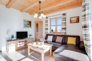 A living room with a wooden ceiling, a television, a sofa, a coffee table, and a window with curtains. - Cosy Apartment "Seeblick" with Garden, Terrace & Wi-Fi (Bad Heilbrunn)