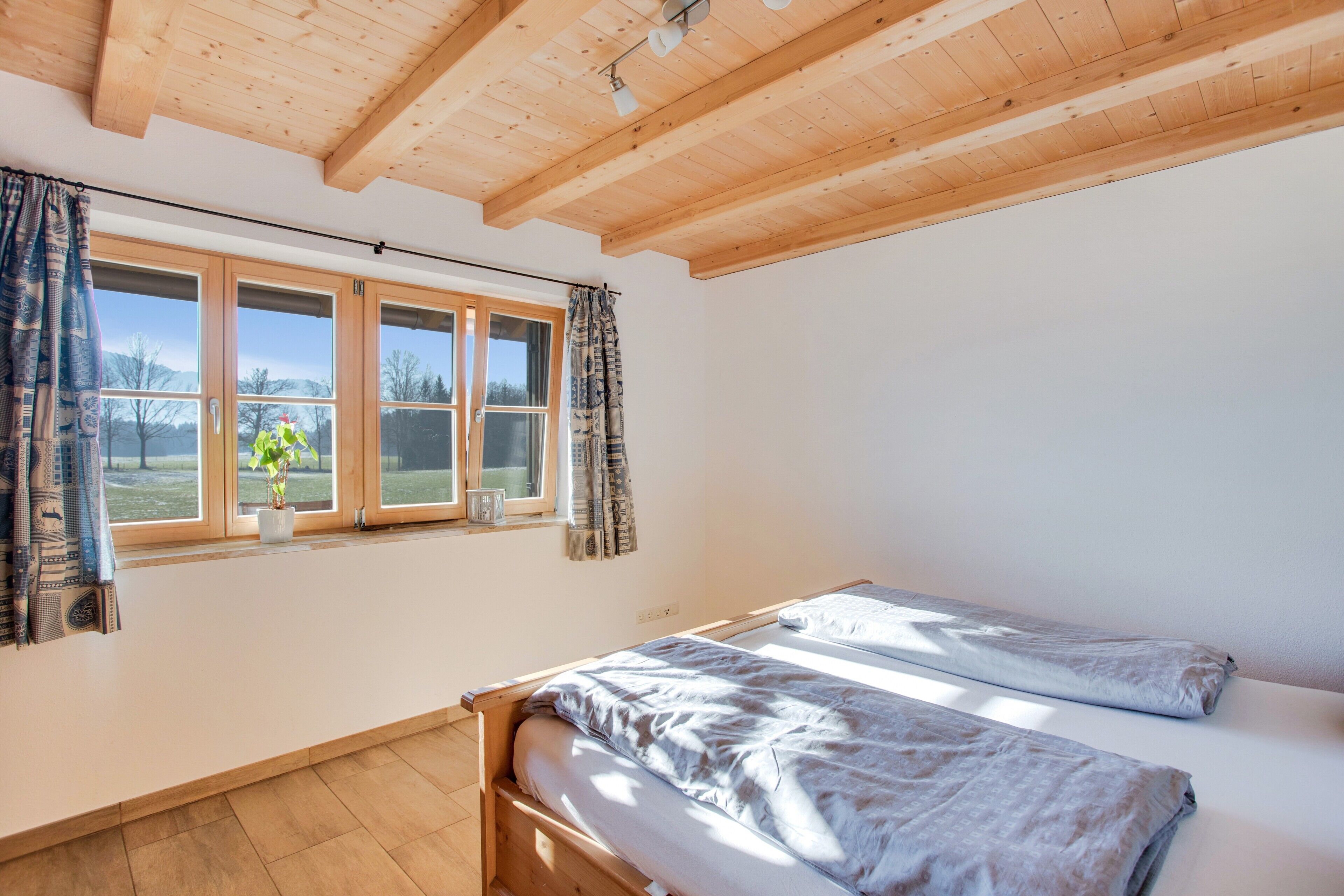 Ein Zimmer mit Holzboden, einem Fenster mit Vorhängen, einem Bett und einer Heizung.