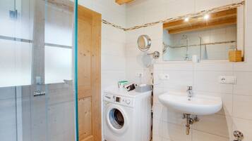 Un baño con mampara de vidrio, lavadora, lavamanos y espejo.