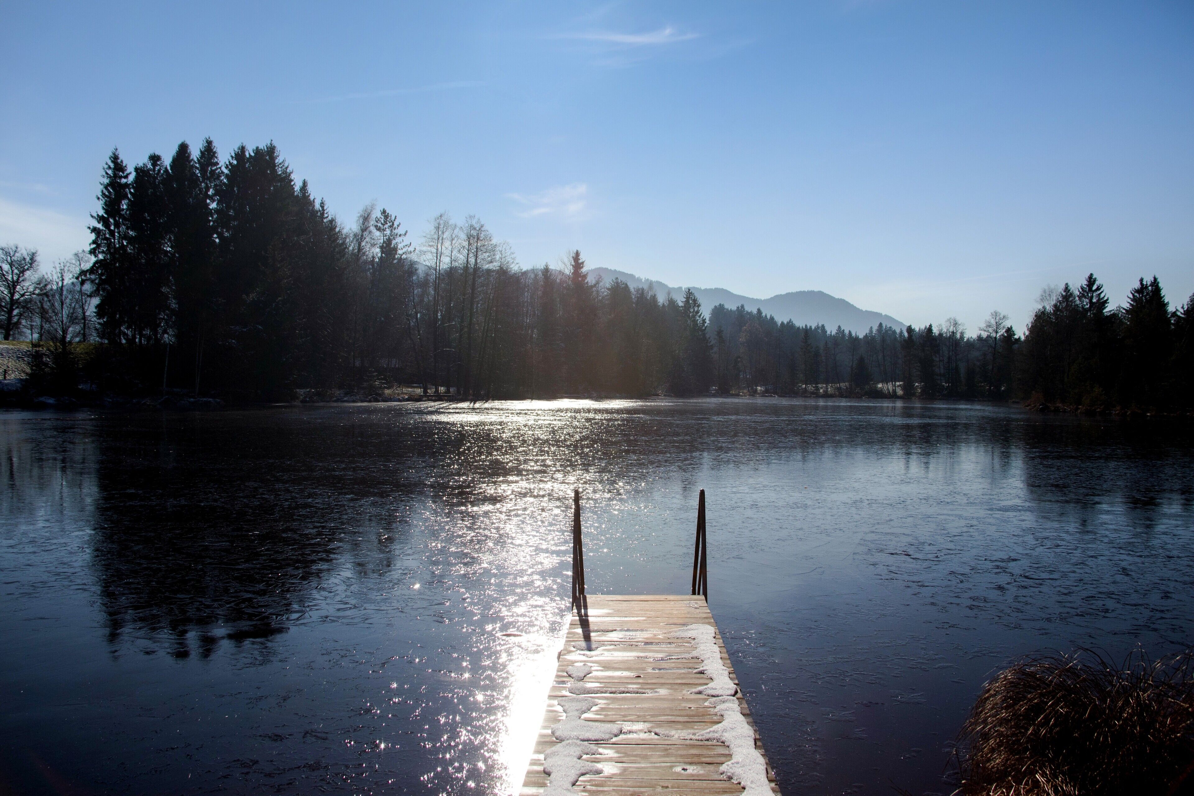 Une jet ée en bois s’étendant sur un lac paisible, où se reflètent les arbres et les montagnes en arrière-plan.