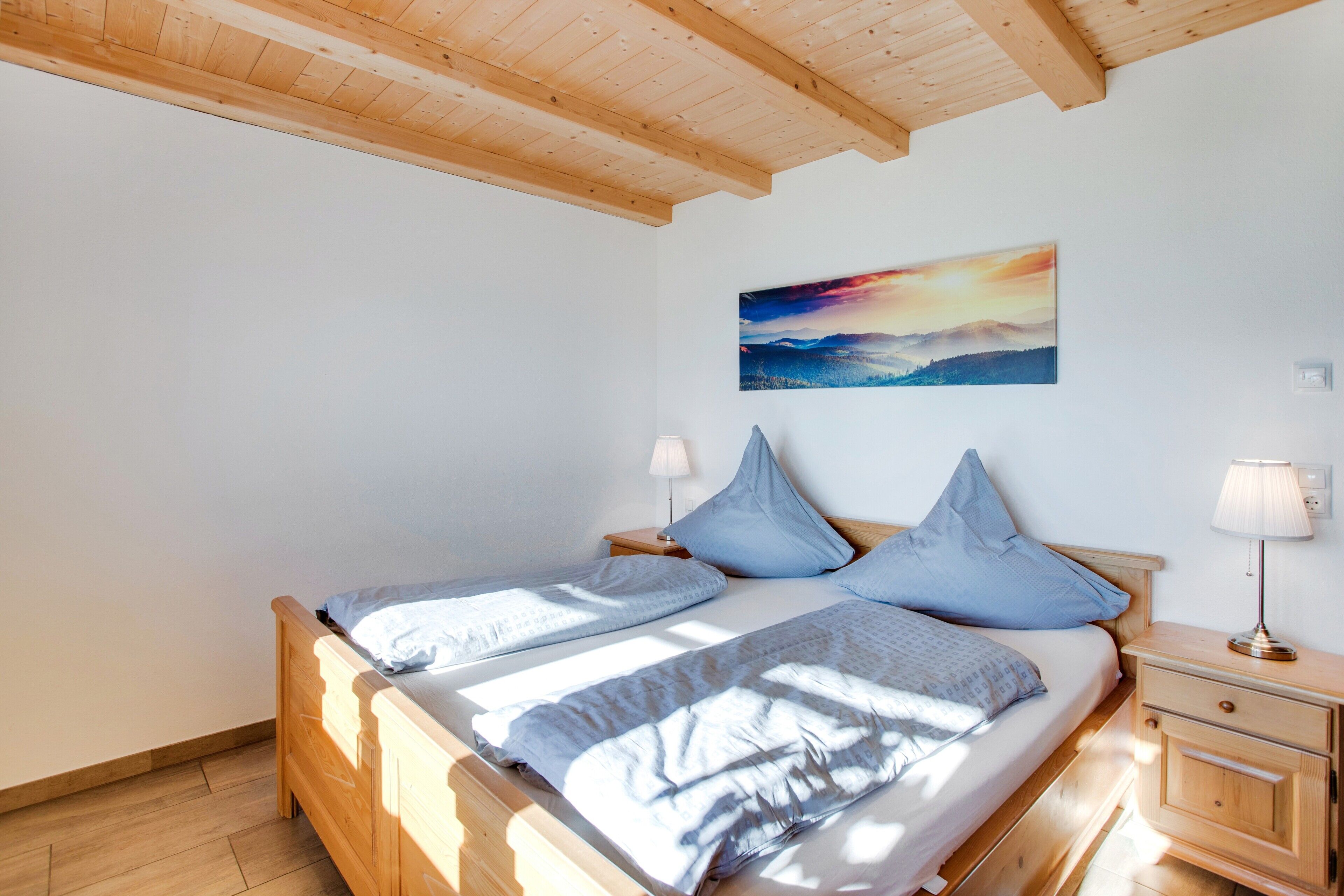 Une chambre à coucher avec un lit en bois, deux tables de chevet, une commode et un tableau accroché au mur.