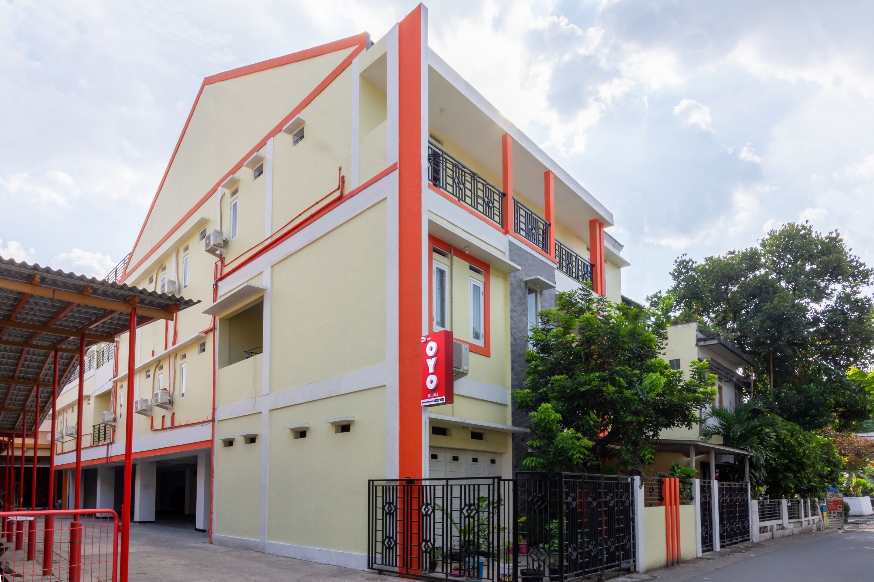 A multi-story building with a red and white facade, balconies, and a gated entrance.