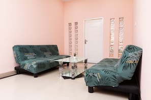 Ein Zimmer mit zwei grünen Sofas, einem Glastisch und dekorativen Wandverkleidungen.