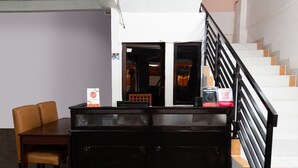 Un comptoir d’accueil avec une table et des chaises en bois, un escalier avec une rampe noire et un mur blanc avec une porte donnant sur une autre pièce.