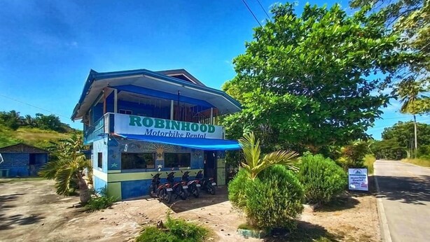 En bygning med et skilt, der siger "ROBINHOOD Motorbike Rental", og flere motorcykler parkeret foran.