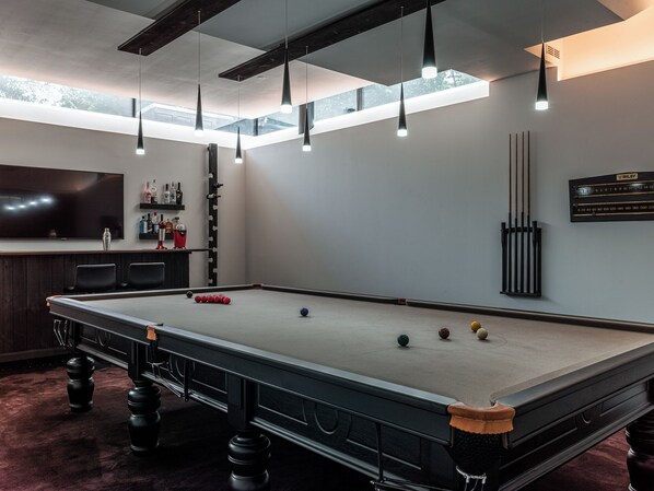A pool table with balls, a bar area with bottles, and a mounted pool cue rack.