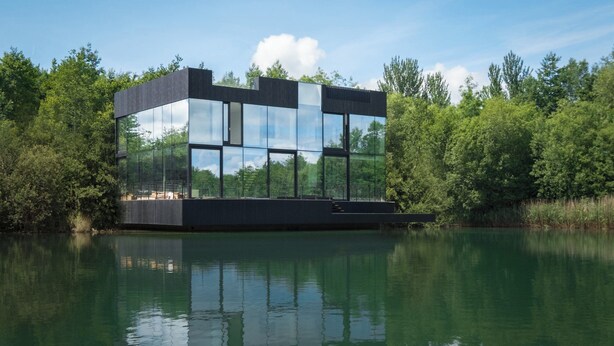 A modern glass house by a calm lake, surrounded by dense greenery. - Gorgeous Lakeside Villa with wellness SPA and 8 seater cinema (Lechlade-on-Thames)