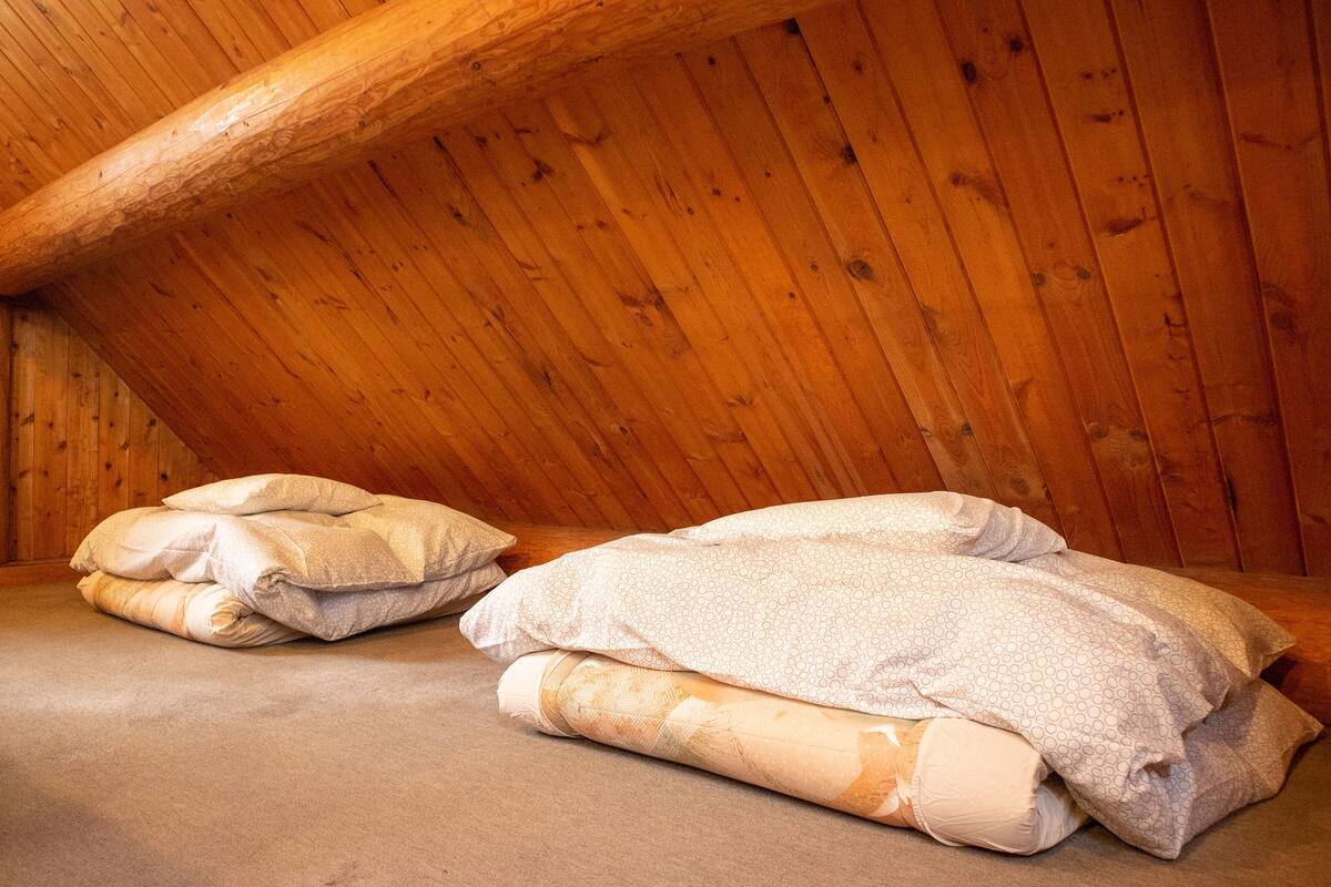 Quarto de sótão acolhedor, com vigas de madeira, teto inclinado e uma cama grande com cobertores dobrados.