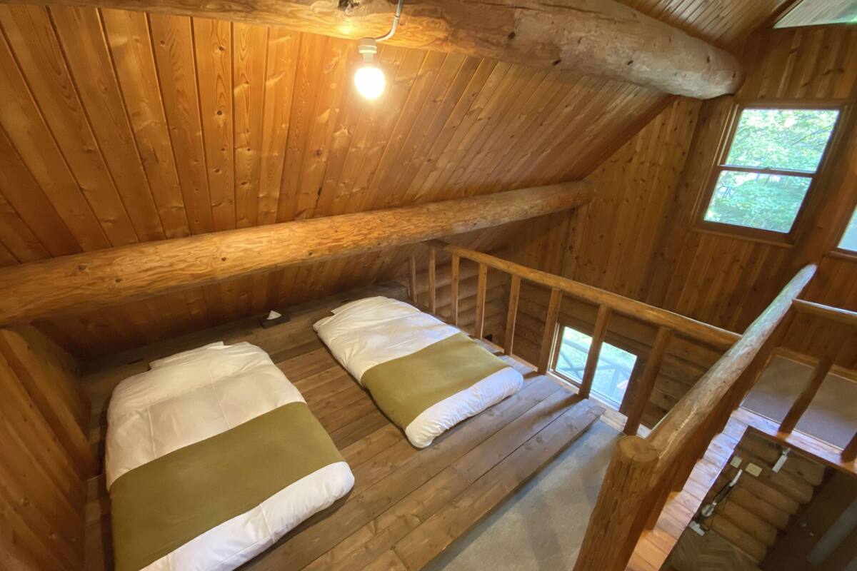 Uma cabana com quarto no mezanino, com duas camas, escada de madeira e janela com vista para o verde.