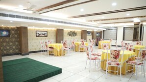 Un'ampia sala da pranzo interna con diversi tavoli rotondi ricoperti da tovaglie gialle e sedie bianche con rivestimenti floreali.