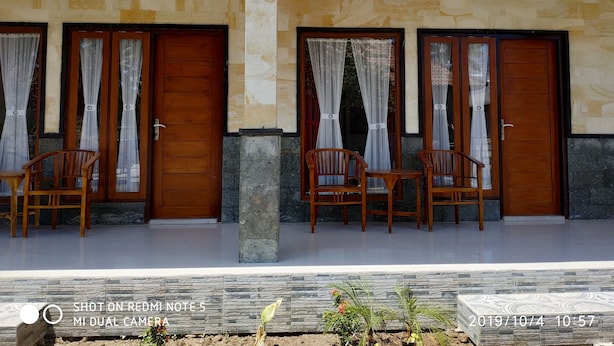 A hotel entrance with two wooden doors, each flanked by a pair of wooden chairs and a table. - Omah Nusa Villa (Penida Island)