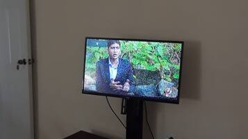 A television on a stand with a wall-mounted clock above it.