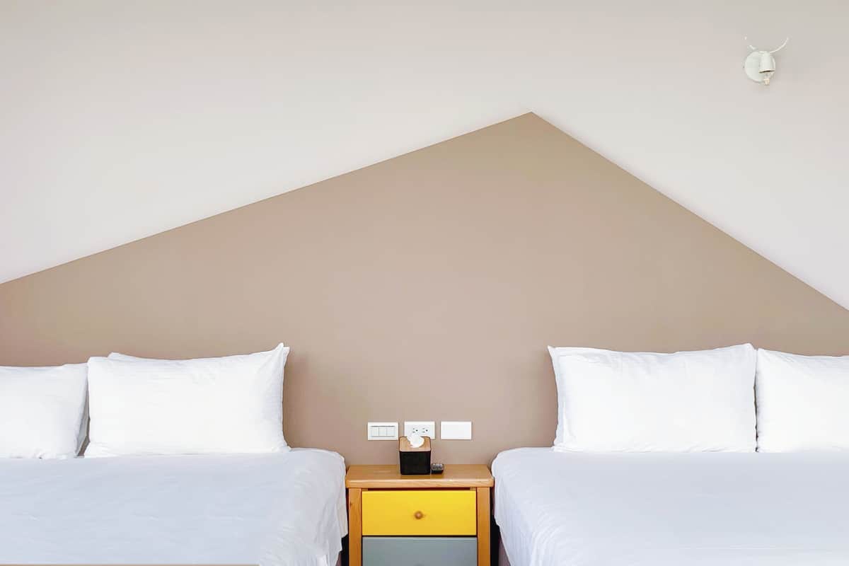 Una habitación con dos camas, una mesita de noche con cajón y un interruptor de luz en la pared.