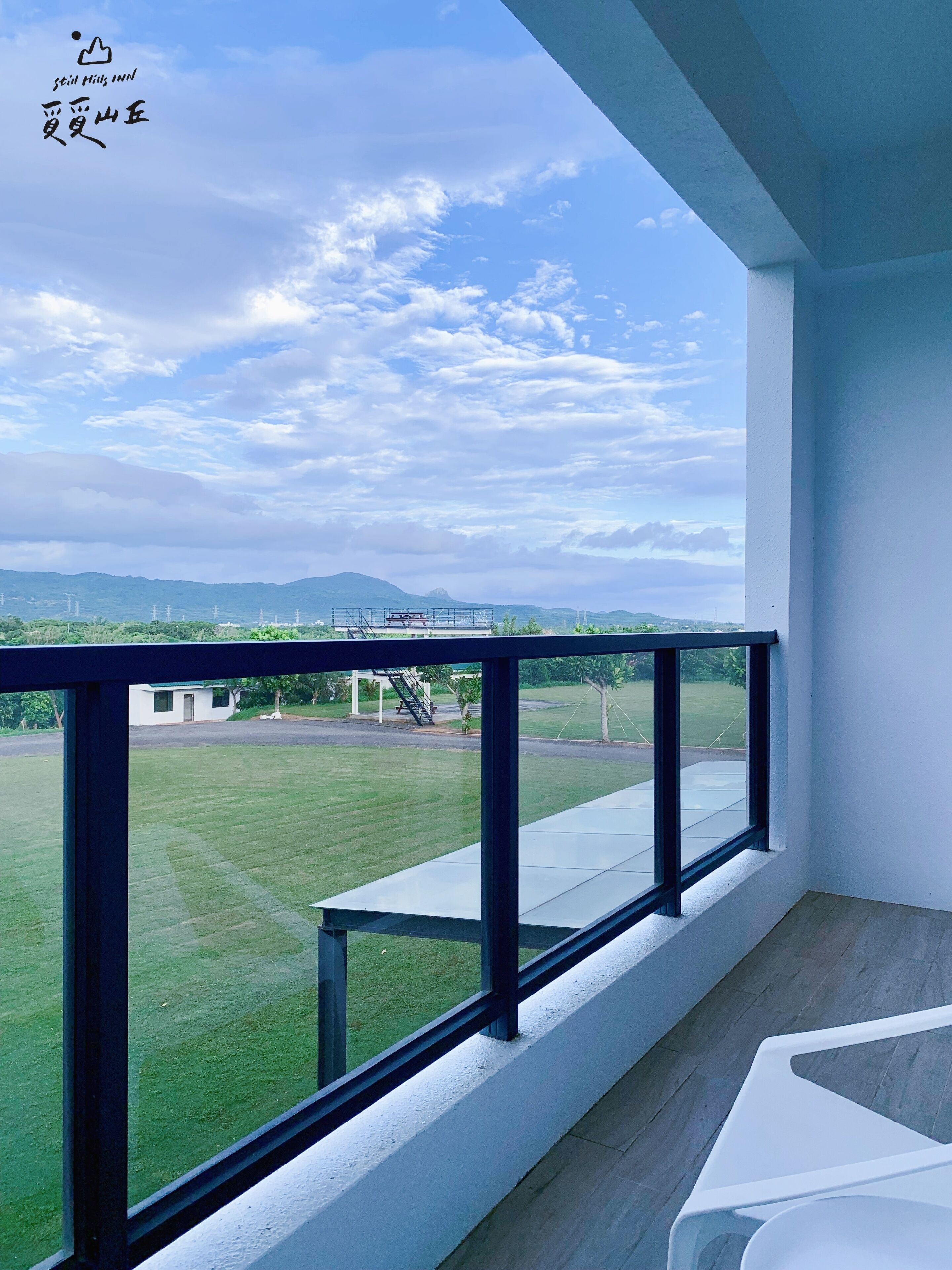 A balcony with a clear view of a grassy area and distant mountains.