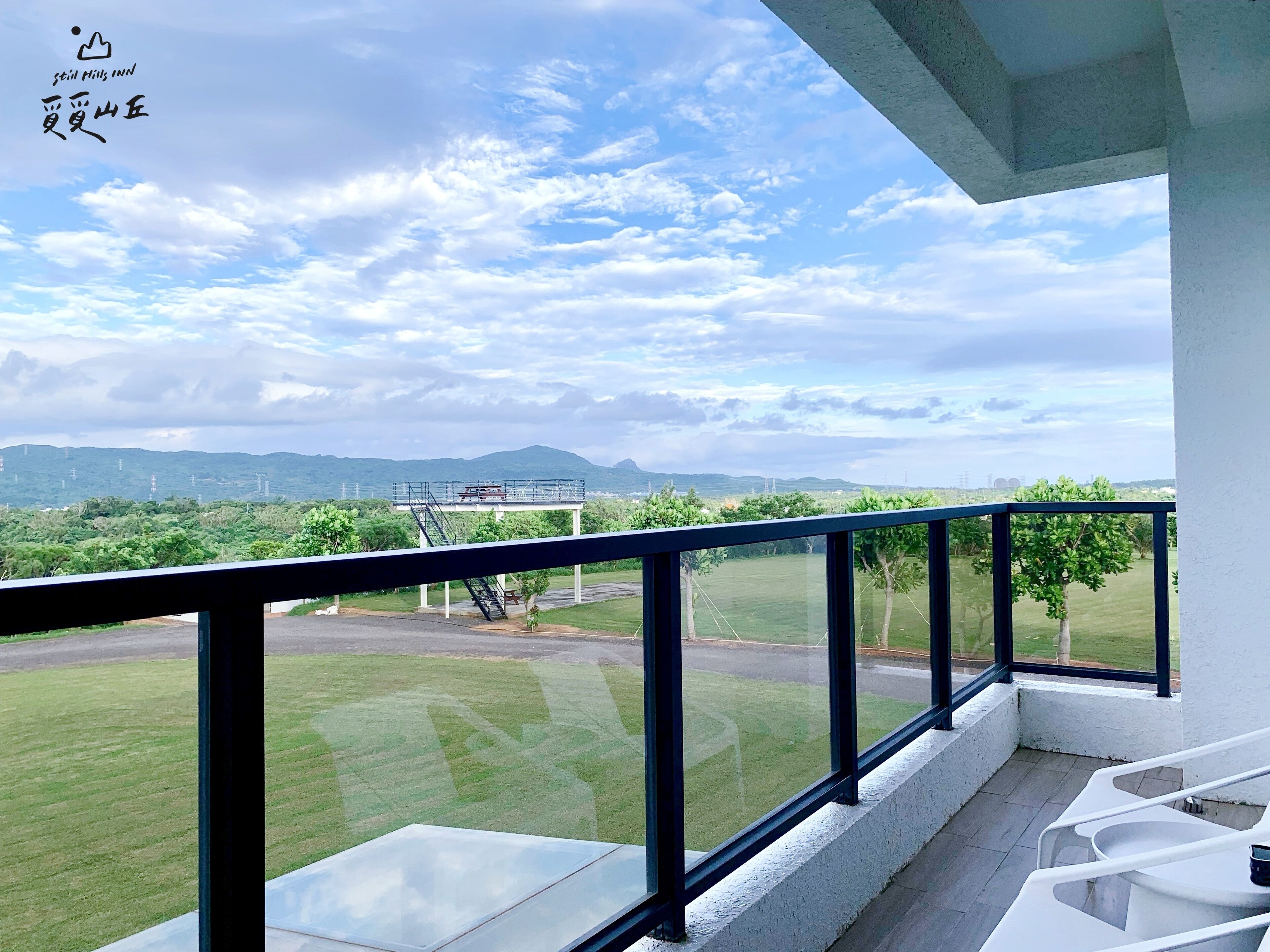 A balcony with a clear view of a grassy area, a road, and distant mountains.