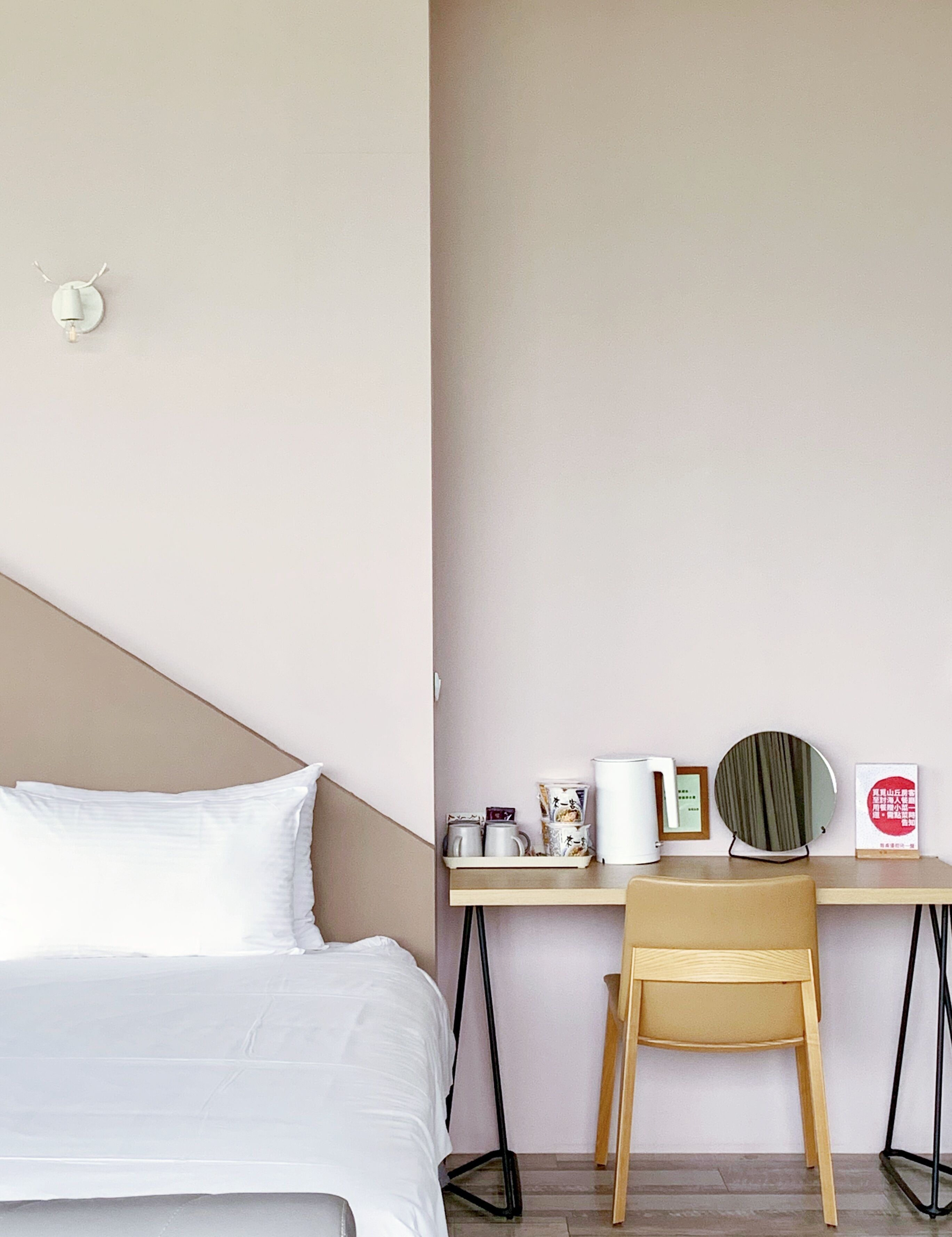 Una habitación de hotel con una cama, un escritorio con una silla, una cafetera, un espejo y un cuadro en la pared.