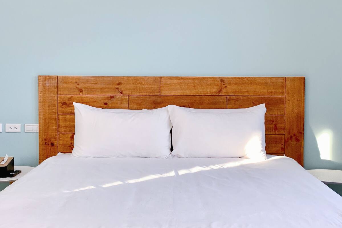 Una cama con cabecera de madera, ropa de cama blanca y una mesita de noche con una caja de pañuelos.