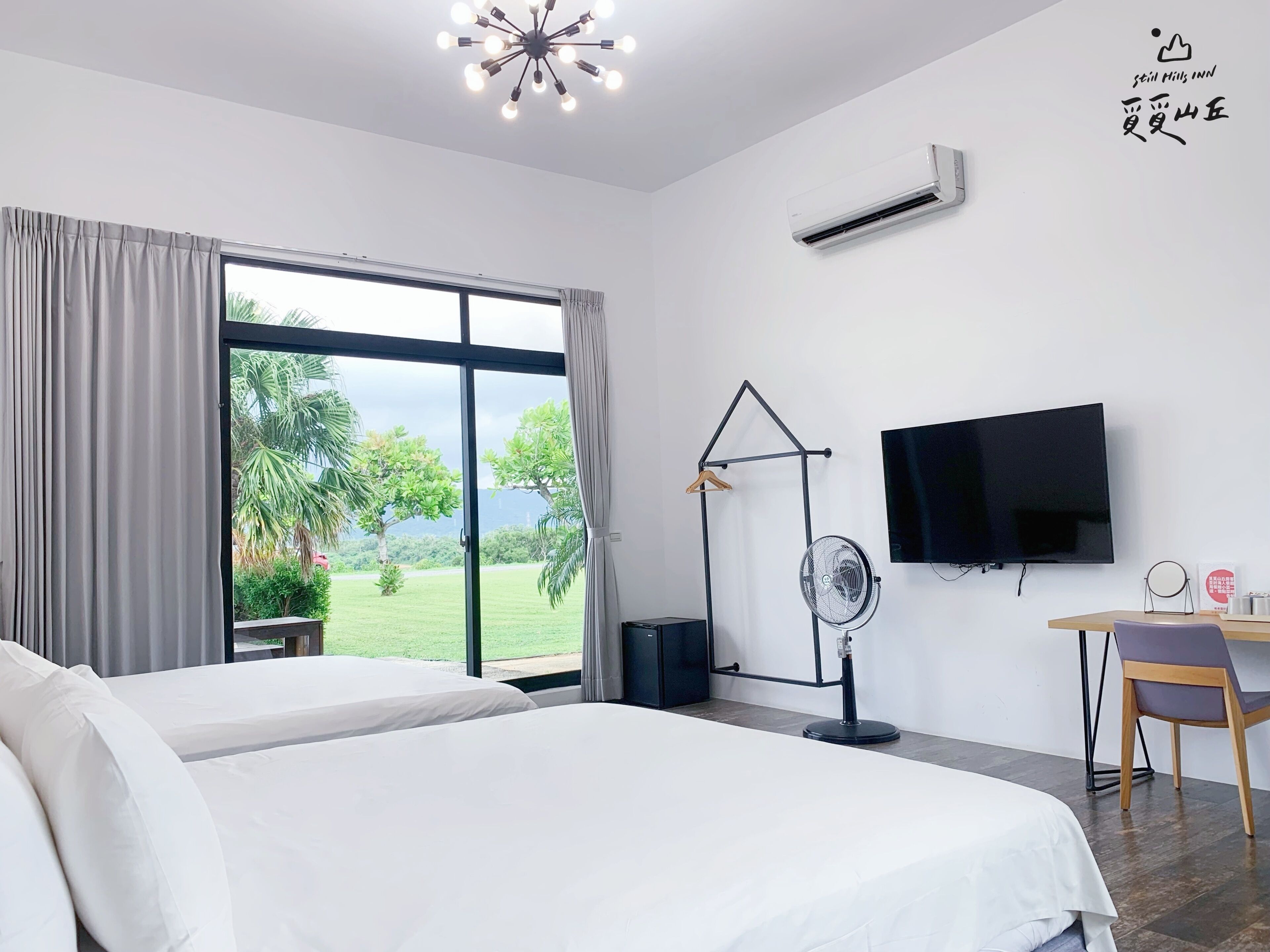 A hotel room with a large bed, a desk with a chair, a TV, and a fan.